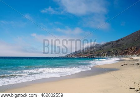 Garrapata Beach In California. Yellow Sand And Blue Misty Sky With Dark Rocks. Travelling On Highway