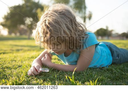 Summer Kids Outdoor Portrait. Happy Child With Magnifying Glass Lying In Grass. Environmental, Ecolo