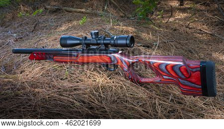 Red Semi-automatic Rimfire Rifle With Scope On A Forest Floor