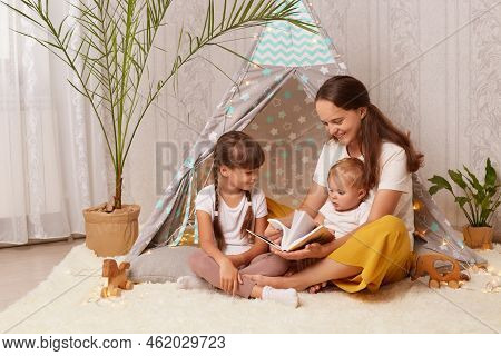 Indoor Shot Of Mother With Two Charming Little Girls Sitting Together In Wigwam, Mom With Her Childr
