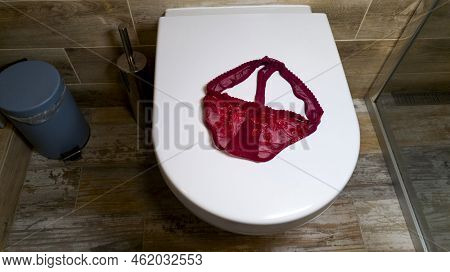 Carelessly Thrown Red Lace Women's Panties Lie On The Toilet. Luxurious Elegant Sexy Women's Thong L