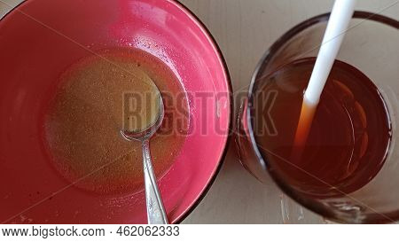 A Red Bowl Used To Eat Soupy Noodles With A Little Gravy In It And A Glass Filled With Leftover Tea.