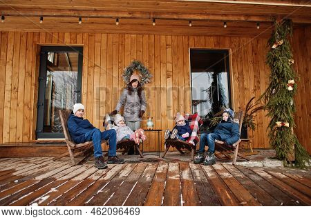 Attractive Mother With Her Four Kids On The Terrace Of A Wooden House  In Winter Day.