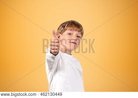 Young Student Wearing Casual Wear Is Showing Thumb Up Gesture In Front Of Empty Orange Wall In Backg