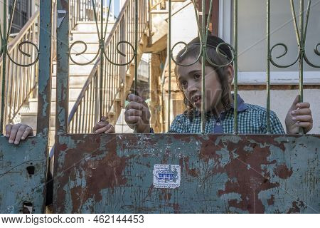 Jerusalem, Israel - July 7th, 2022: An Orthodox Jewish Boy Looking Out Behind The Gates Of His Commu