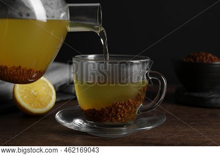 Pouring Buckwheat Tea Into Cup On Wooden Table, Closeup