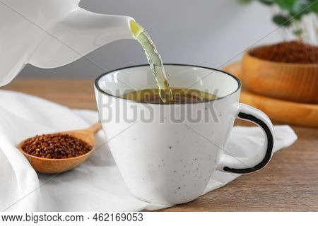 Pouring Buckwheat Tea Into Cup On Wooden Table, Closeup