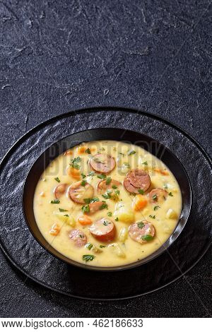 Kartoffelsuppe, German Potato Soup With Sausages In Black Bowl On Dark Concrete Table, Vertical View