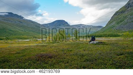 Female Hiker With Heavy Gear Sitting On A Boulder, Overlooking Vast Arctic Valley Rapadalen In Sarek
