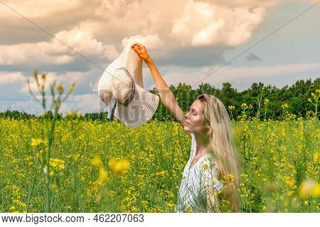 Beautiful Girl Holding Wide-brimmed Hat In A Flowering Field In White Dress. Sunbeams, Glare, Light 