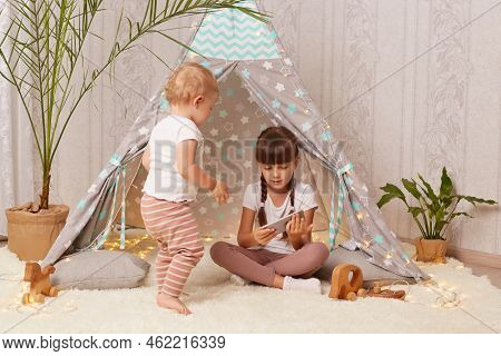 Indoor Shot Of Pretty Adorable Little Girls Wearing White T Shirts Sitting On Floor In Shelter And P