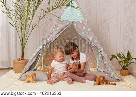 Indoor Shot Of Smiling Adorable Little Girls Wearing White T Shirts Sitting On Floor In Peetee Tent 