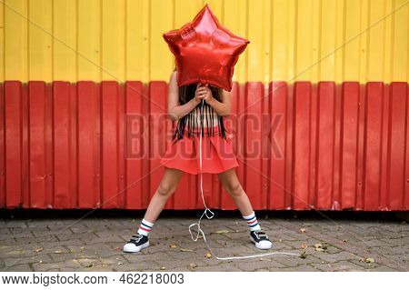 A Stylish Fashionable Girl In Striped Leggings And Sneakers Covers Her Face With A Red Balloon In Th