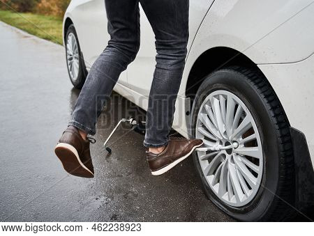 Close Up Of Male Auto Mechanic Standing On Metal Wrench While Unscrewing Lug Nuts On Car Wheel. Youn