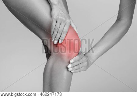 Young Woman Suffering From Knee Pain, Pressing Hands To Sore Spot, Highlighted In Red, Black And Whi