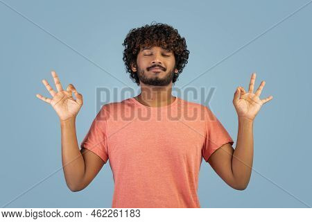 Peaceful Indian Guy Meditating Over Blue Stdio Background