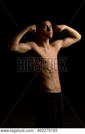 Shirtless 19 Year Old Teenage Boy Flexing His Arms With A Black Background
