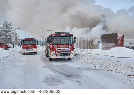 Saariselka, Finland - Circa 2022: Fire trucks at a burning down of shopping center Kuukkeli in Finnish Lapland. Firefighters trying to stop the spreading flames, emergency light signalson