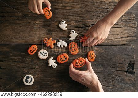Hands Reach For Halloween Gingerbread In Form Of Ghosts, Pumpkins And Gingerbread Man On Wooden Back