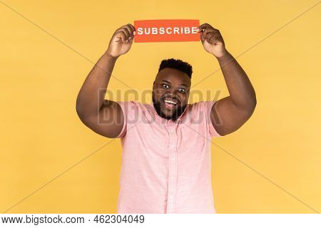 Portrait Of Excited Amazed Man In Pink Shirt Holding With Paper Card With Subscribe Inscription Abov