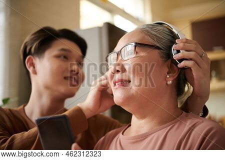 Smiling Senior Woman Enjoying Listening To Music In Heaphones That Grandson Presented Her