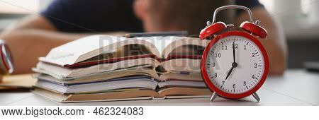 Close-up Of Tired Student Take Nap Behind Pile Of Textbooks On Table. Sleepy Man Resting During Educ