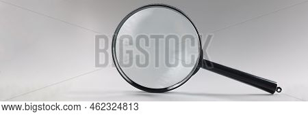 Close-up Of Single Magnifying Glass With Black Handle, Leaning On Grey Surface. Simple Design Of Len