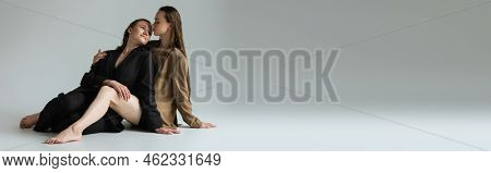 Young And Cheerful Lesbian Couple In Beige And Black Blazers Sitting And Looking At Each Other On Gr
