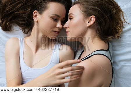 Top View Of Young And Pretty Lesbians In Underwear Looking At Each Other On Bed.