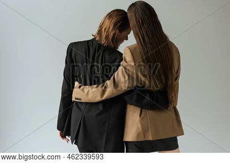 Back View Of Lesbian Women In Black And Beige Blazers Embracing Isolated On Grey.