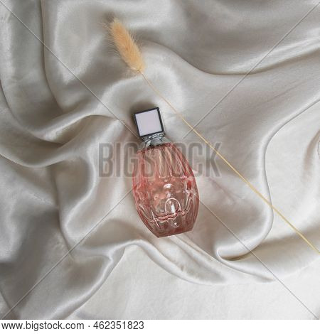 A Bottle Of Perfume In Pink Glass On A Background Of Silk Fabric. Minimalistic Fashion Photography