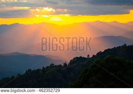 Aerial View Of Dramatic Orange Sunlight Shining Through Clouds To Blue Mountain Ranges Of Tropical R