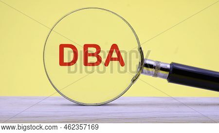 Dba Text On A Yellow Background Through A Magnifying Glass. Concept Photo.