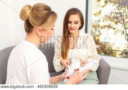 Beautician Offering Product For The Young Woman Holding White Plastic Bottles With A Cream Sitting O