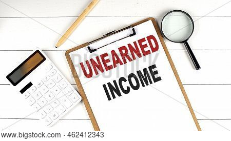 Unearned Income Words On Clipboard, With Calculator, Magnifier And Pencil On The White Wooden Backgr