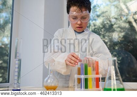 Confident Smart Caucasian Boy Wearing Safety Goggles And White Lab Coat, Learning Chemistry In The S