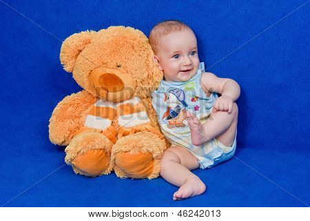 Fünf Monaten kleiner Junge sitzt neben einem Teddybär