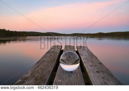 Glass Ball On A Wooden Pier At A Swedish Lake At Evening Hour. Nature Shot From Scandinavia