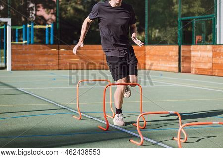Blond Boy In Sportswear Jumps Over Red Obstacles To Improve Lower Body Dynamics. Plyometric Training