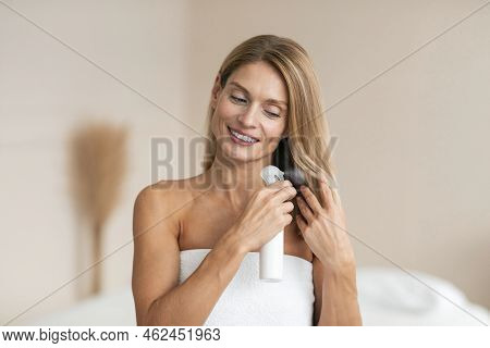 Hair Care Treatment. Middle Aged Woman Spraying Hairspray, Moisturizing Hair After Shower Standing W