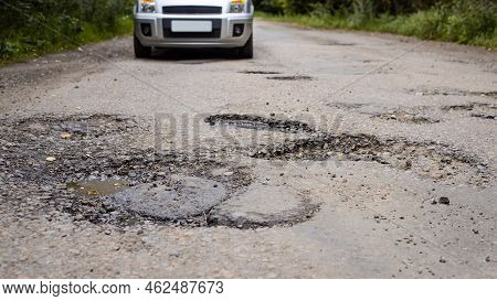 Wide Picture Of A Car Approaching Part Of A Road In Poor Condition With Lot Of Holes And Chuckholes