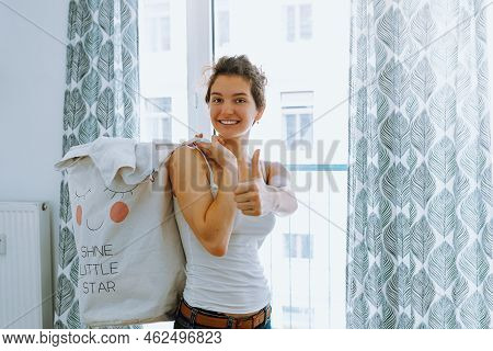 Happy Teenage Girl With Smile, Holds Filled Dirty Laundry Basket, Shows Thumbs Up Hand Sign. Cleanin