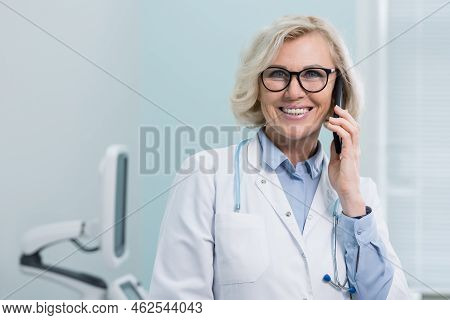 Young Woman General Practitioner Provides Telephone Consultation At Break. Blonde Woman In White Coa