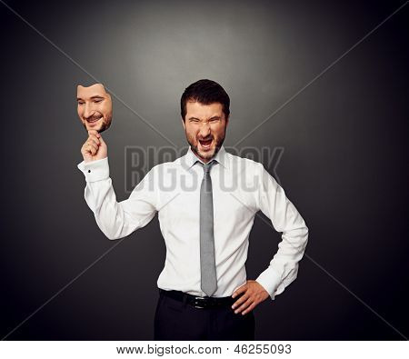 empresário wrathful segurando a máscara com rosto sorridente