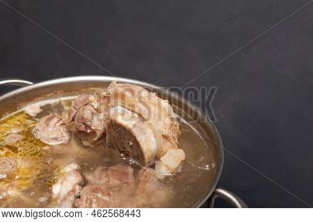 Homemade Beef Bone Broth Is Cooked In A Pot On Dark Background. Bones Contain Collagen, Which Provid