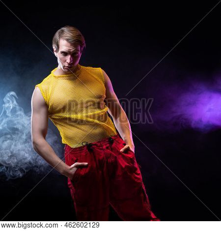 A Young Muscular Man In A Bright Outfit Poses In A Pretentious Pose, Style And Grotesque. Attractive