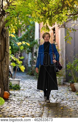Attractive Thirty Year Old White Woman In A Long Dress Walking Down A Narrow Street With Cobble Ston