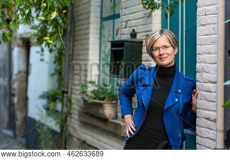 Portrait Of An Attractive Thirty Year Old White Woman Posing At A Traditional White And Green Facade