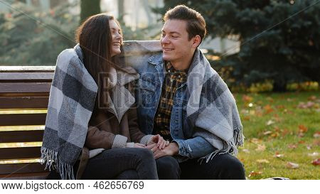 Cute Loving Couple Sit On Bench Warming Each Other Covering Wool Blanket Outdoors In Cold Froze Autu
