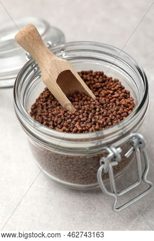 Glass Jar With Wooden Scoop And Buckwheat Tea Granules On Light Grey Table, Closeup